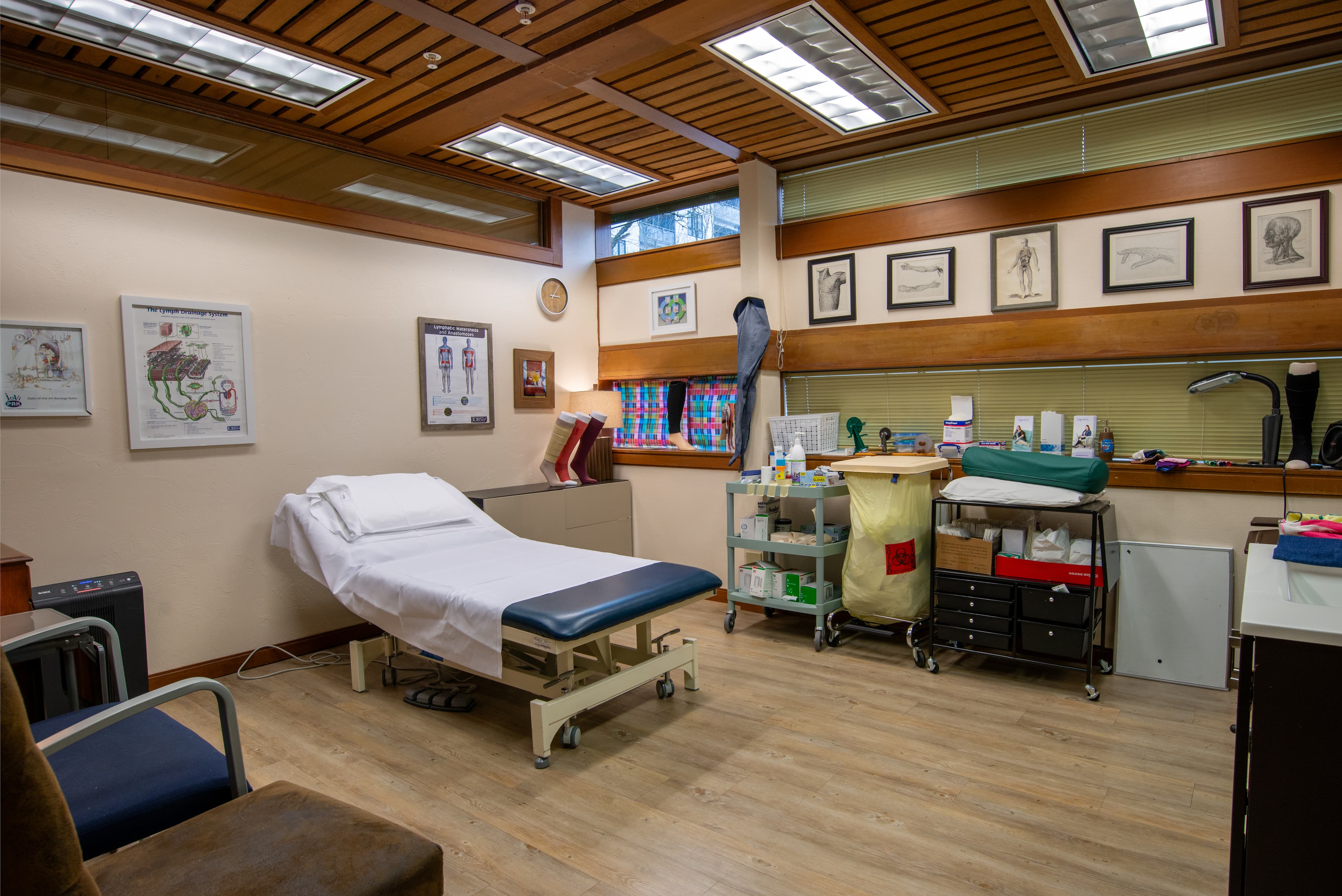 A private treatment room with a pneumatic hi-lo and a bariatric chair, anatomical references, medical supplies, and demonstrations of compression socks adorn the room.